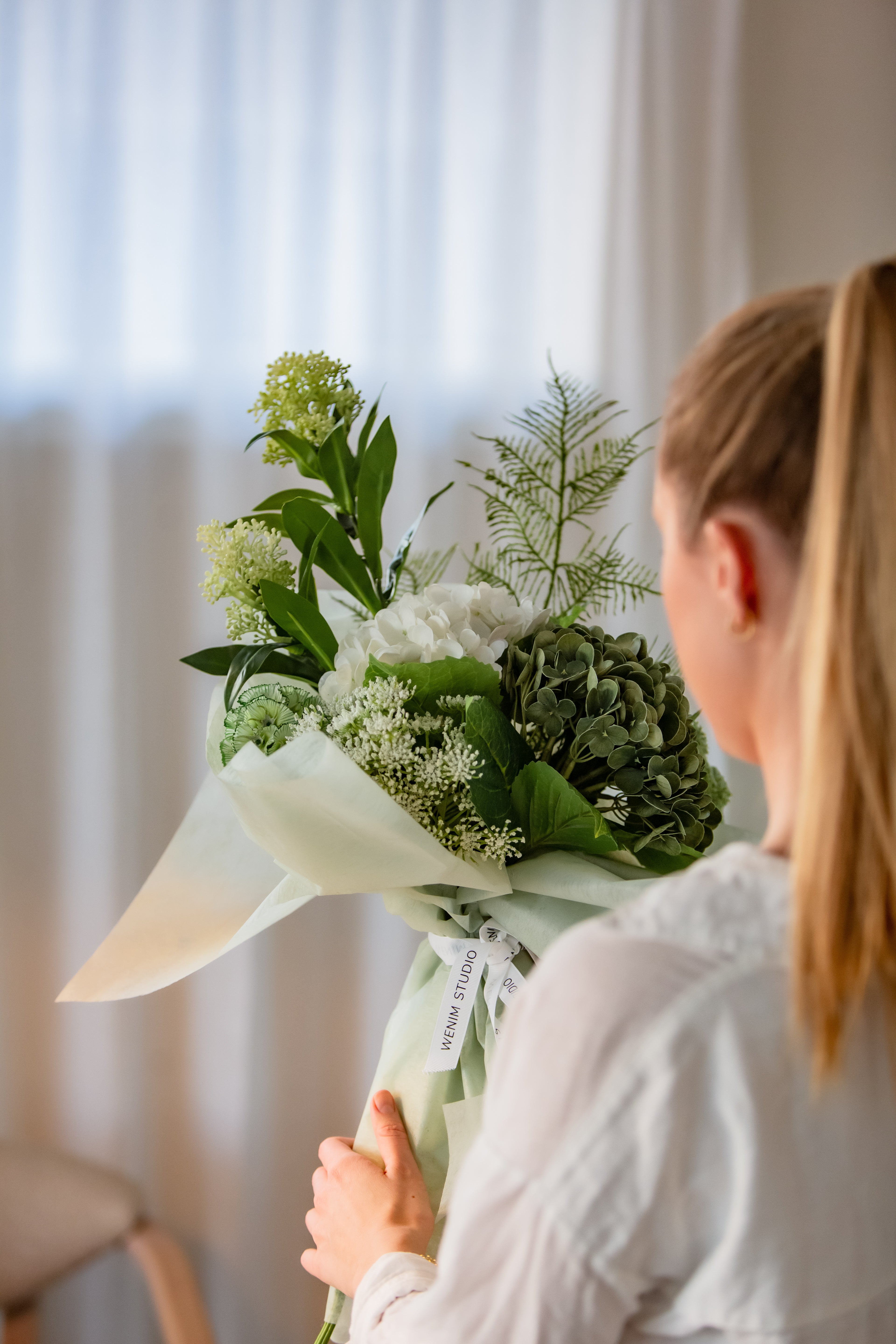 Person holder kunstig bukett med grønne og hvite blomster